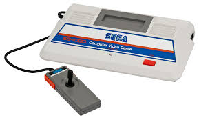 Sega Sg-1000, Primera Consola Doméstica De Sega Lanzada En 1983, Con Diseño Blanco Y Azul Y Mando Con Joystick.